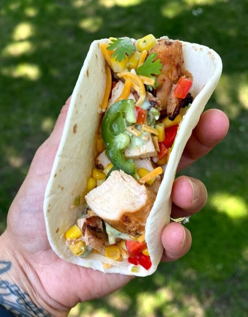 Hand holding a taco with beer marinated grilled chicken and corn salsa